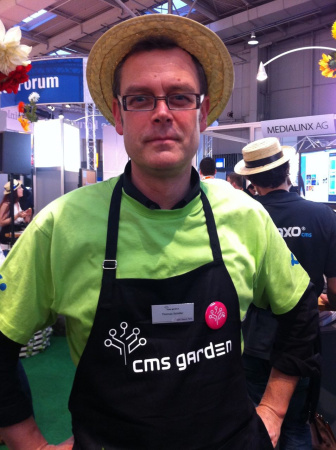 Portrait of a man in a lime-green t-shirt wearing a straw hat and a gardener's apron with CMS Garden logo