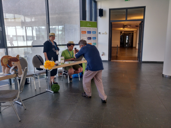 CMS garden info desk in a large foyer, two ambassadors with straw hat, Stephan is taking a picture