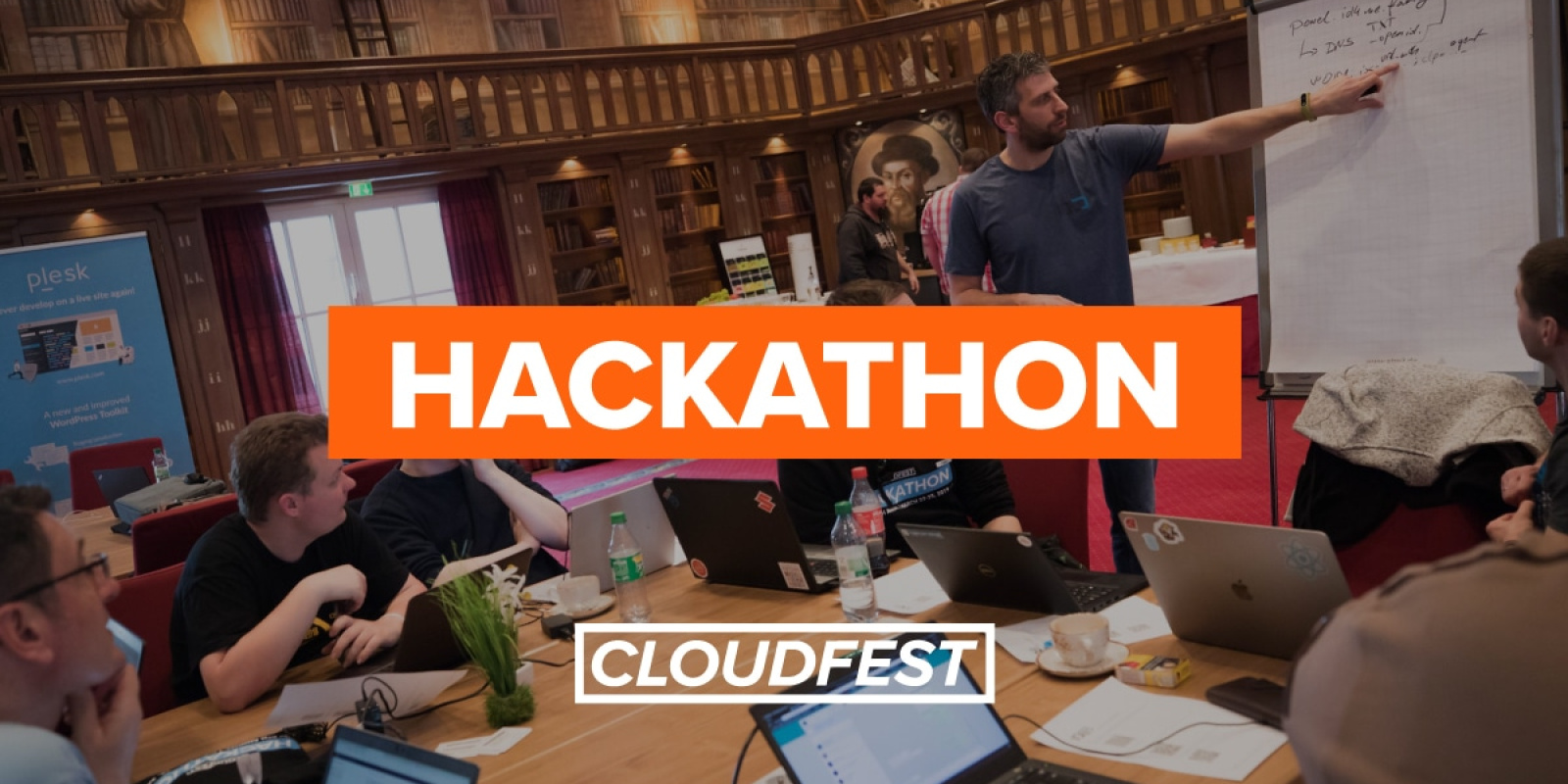 Photo of attendees in a vintage library room, on man is pointing at a flip chart. Overlay wording: Hackathon CloudFest