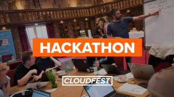 Photo of attendees in a vintage library room, on man is pointing at a flip chart. Overlay wording: Hackathon CloudFest